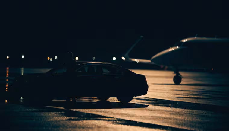 A chauffeur waiting beside a car at a private terminal at night